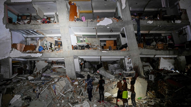 TOPSHOT - People stand in the rubble near a damaged building following an earthquake in Catia La Mar, La Guaira State, some 30kms north-west of Caracas, early on June 25, 2026. Powerful twin earthquakes have killed 32 people and injured more than ...